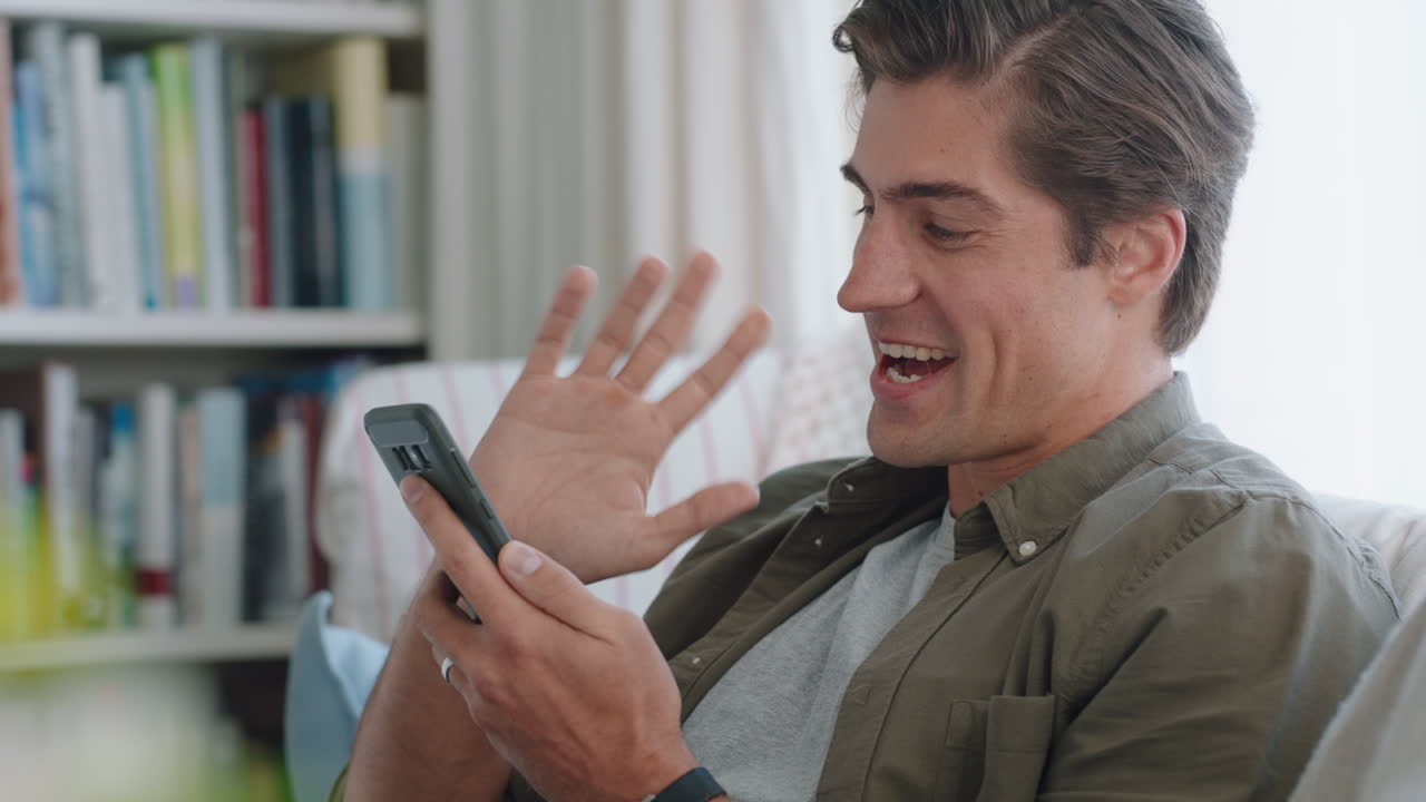 joven atractivo que tiene video chat usando un teléfono inteligente disfrutando de chatear con un amigo en línea compartiendo estilo de vida relajándose en casa imágenes 4k
