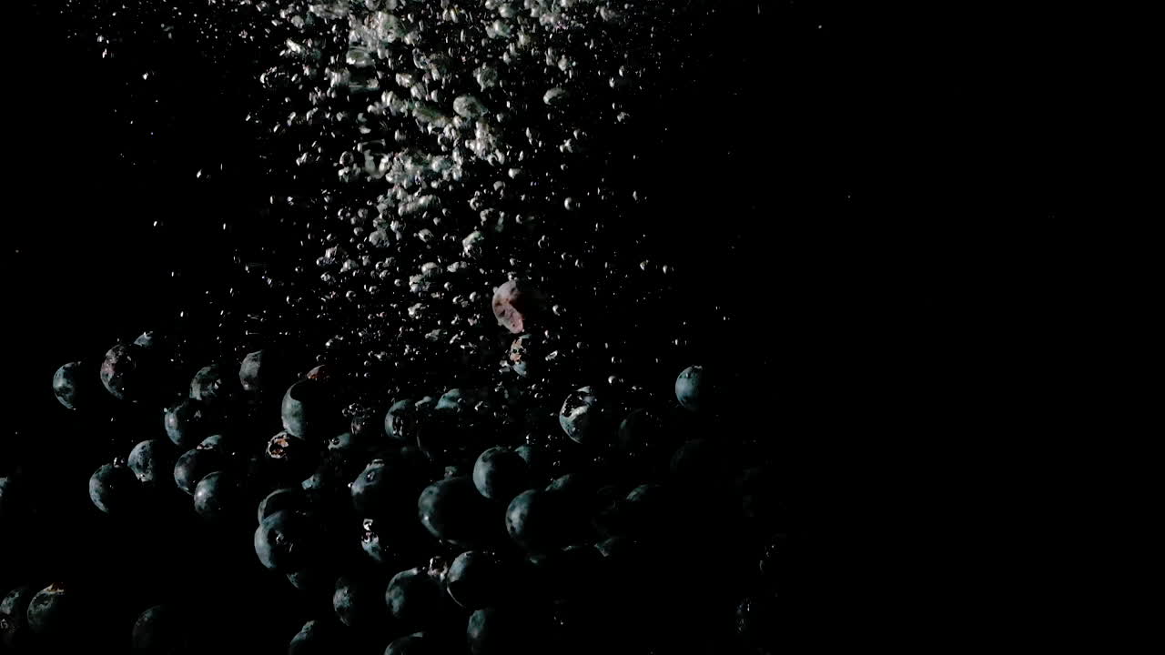 Blueberries dropped into water on black background, slow motion close up