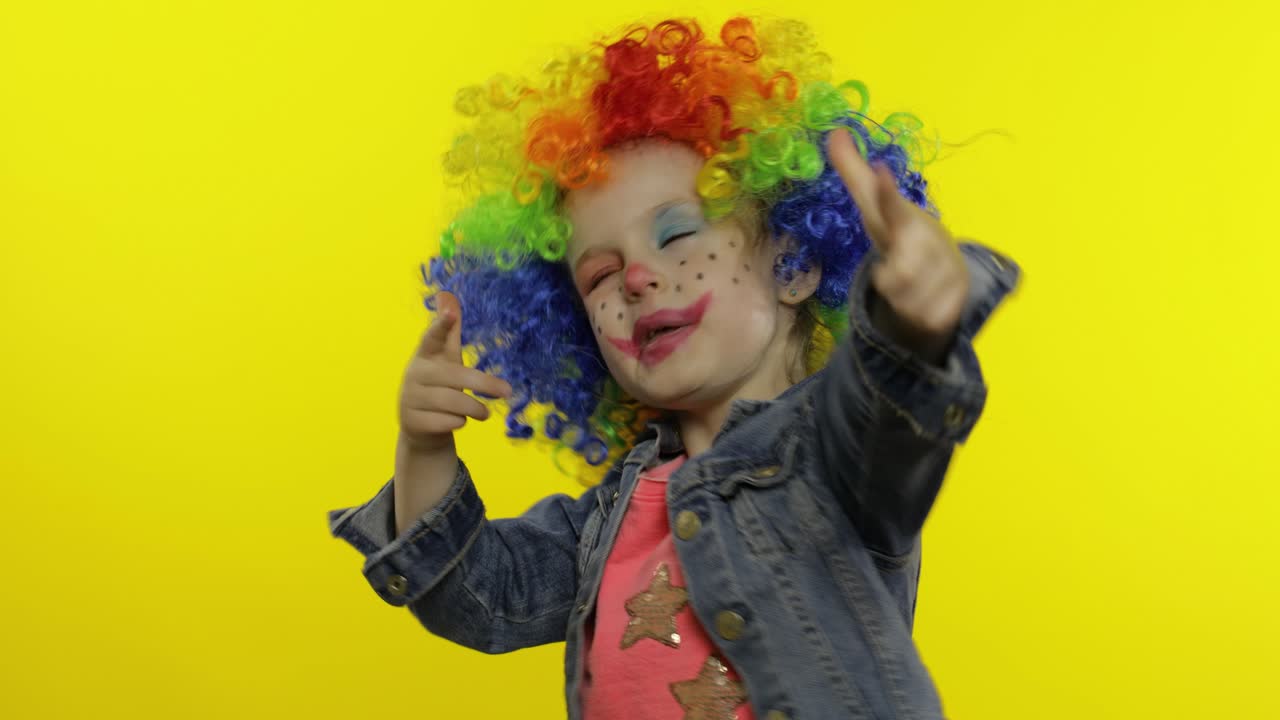 niña pequeña payaso en peluca colorida haciendo caras tontas, tonto alrededor, sonriendo, bailando. halloween
