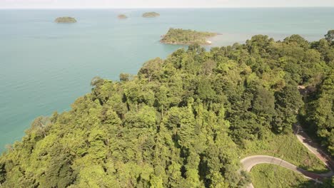 Vuelo-Aéreo-Sobre-La-Jungla-Tropical-Con-Camino-Ventoso,-Océano-E-Islas-Tropicales-A-Distancia