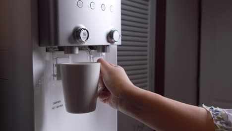 la mujer presiona una taza de agua caliente del purificador de agua y la vuelve a poner