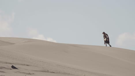 a robed figure struggles across a vast sand dune, then falls to their knees in exhaustion. post-apocalyptic, sci-fi, or fantasy concept of despair, struggle, and survival