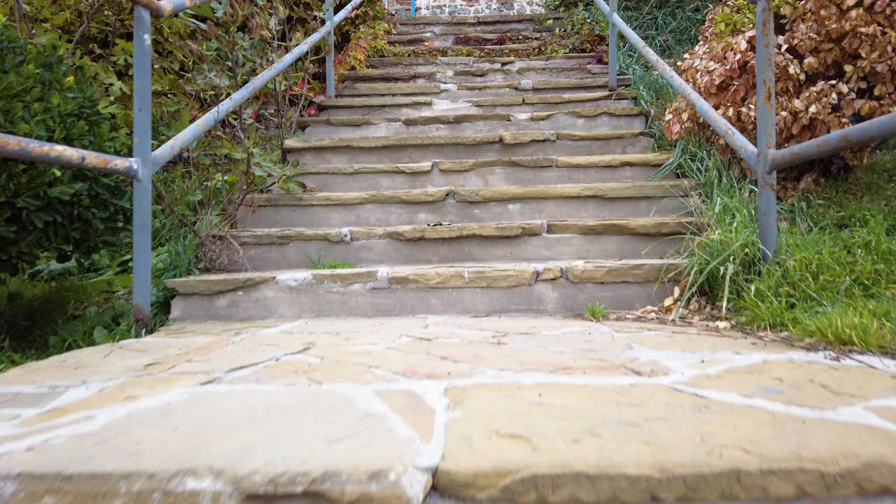 Climbing outdoor straight old stone steps with metal railing of an open panoramic platform. Green and orange vegetation around. No people. Slow motion.