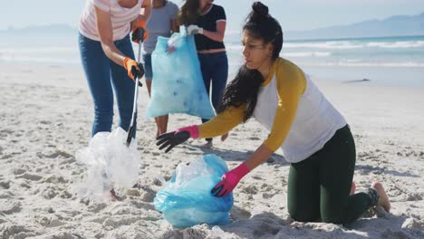 Diverse-group-of-female-friends-putting-rubbish-in-refuse-sacks-at-the-beach