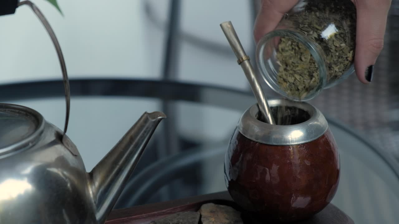 mano de mujer vertiendo yerba en mate para preparar la bebida de infusión local en argentina y uruguay