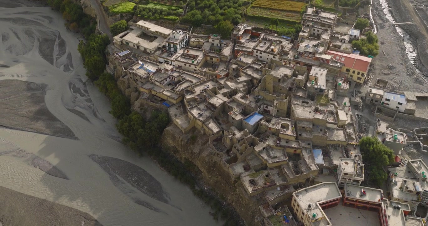 Pueblo de Kagbeni, Mustang, Nepal, toma de dron alejándose de casas tradicionales agrupadas construidas al borde de un acantilado para revelar los extensos y trenzados cauces del lecho del río Kali Gandaki.