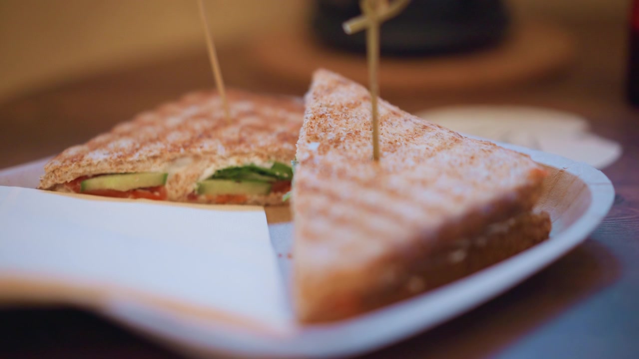Primo piano di un sandwich grigliato tagliato a metà con ingredienti visibili come cetriolo, pomodoro e lattuga su pane integrale. La scena include un'illuminazione soffusa che evidenzia i dettagli della texture.