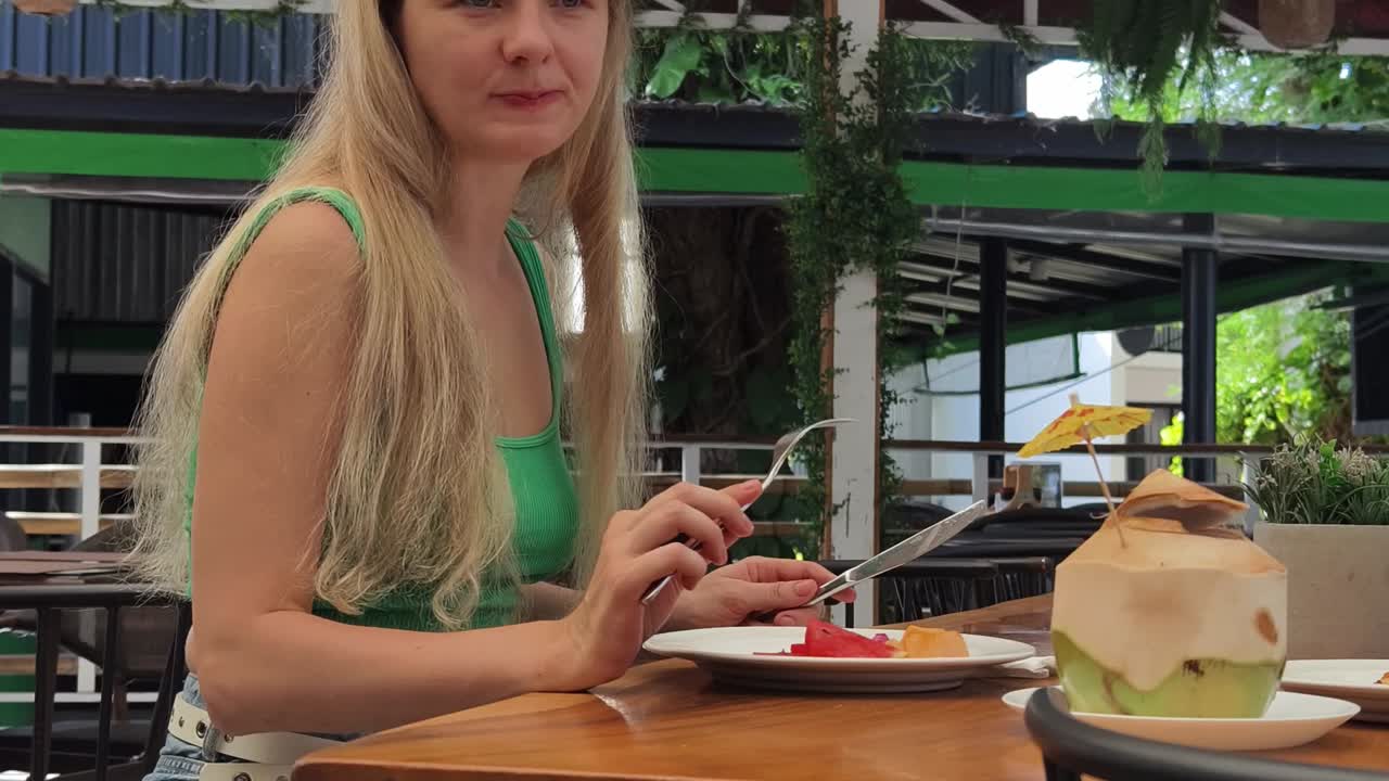 mujer comiendo ensalada de frutas frescas y coco en un restaurante tropical
