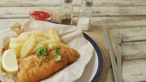 Vídeo-De-Pescado-Y-Patatas-Fritas-En-Un-Plato,-Sal-Y-Pimienta-Y-Ketchup-En-Una-Mesa-De-Madera