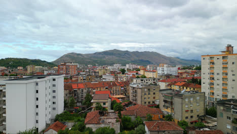 Aerial-drone-tilt-up-shot-over-city-buildings-with-mountains-in-the-background-in-Shkodra,-also-known-as-Shkoder-or-Scutari-along-the-northwestern-Albania