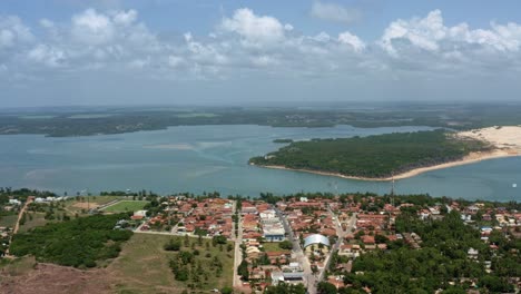 Dolly-out-aerial-drone-extreme-wide-shot-of-the-tropical-beach-town-of-Tibau-do-Sul-in-Rio-Grande-do-Norte,-Brazil-with-the-Malembá-Sand-Dunes,-Atlantic-Ocean,-and-Guaraíras-Lagoon-in-the-background