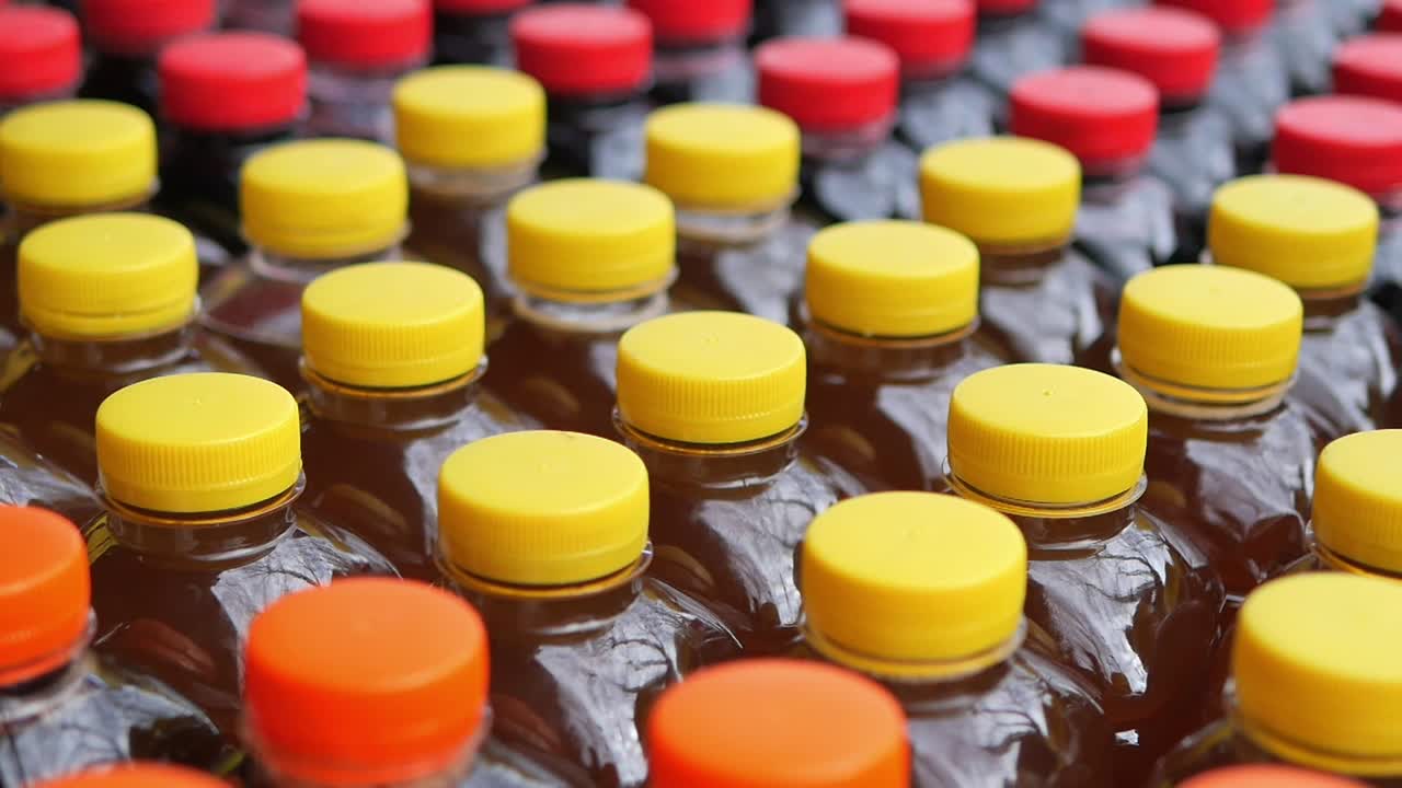 Rækker af plastikflasker med farverige gule, røde og orange låg.