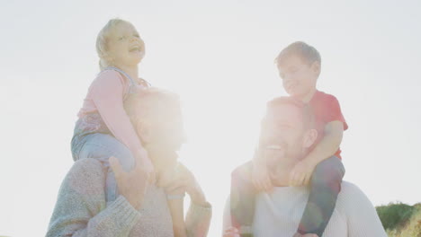 grandfather and father giving granddaughter and son ride on shoulders against flaring sun