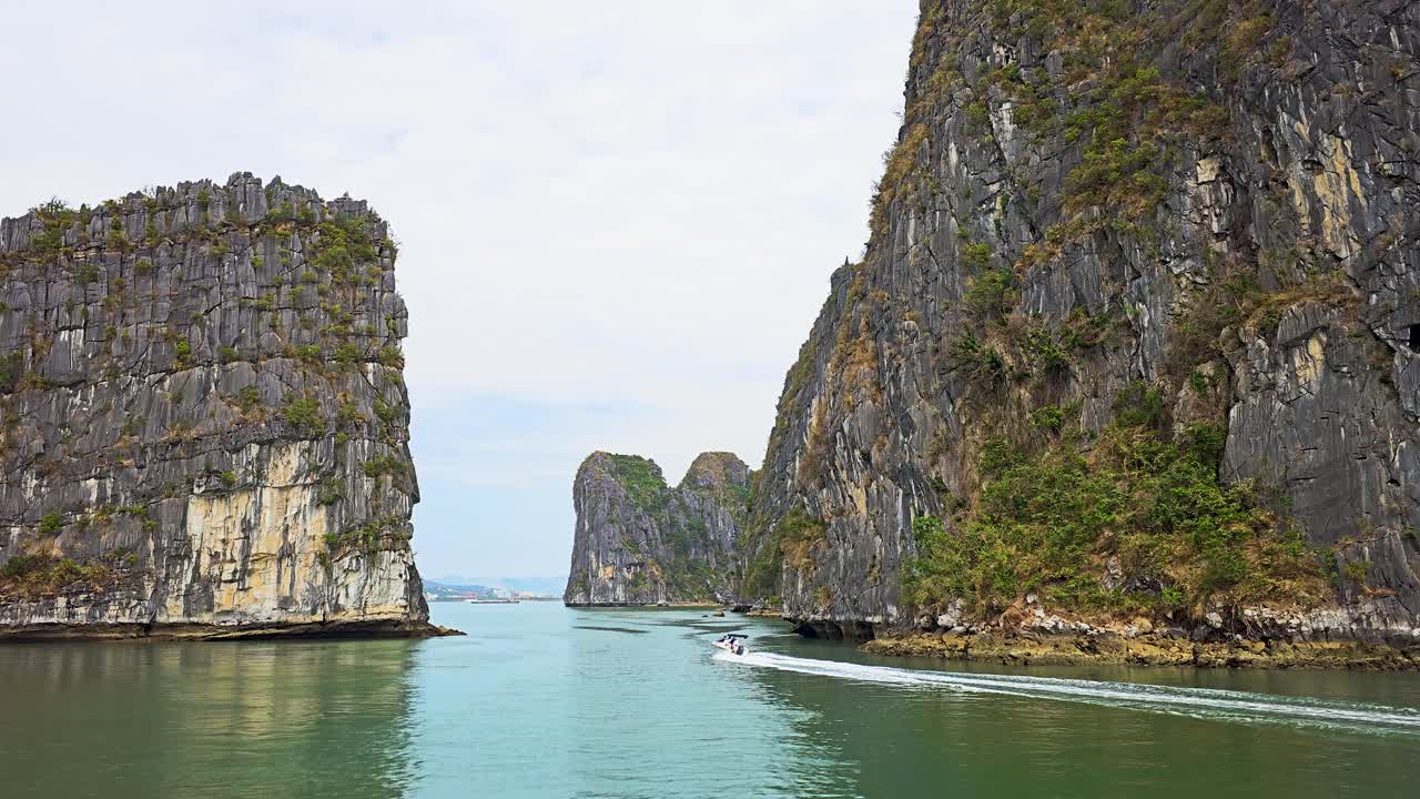 Towering limestone karsts rise dramatically from the emerald waters of Ha Long Bay in Vietnam, creating a stunning natural gateway while a small motor boat navigates through the tranquil passage