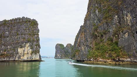 towering limestone karsts rise dramatically from the emerald waters of ha long bay in vietnam, creating a stunning natural gateway while a small motor boat navigates through the tranquil passage