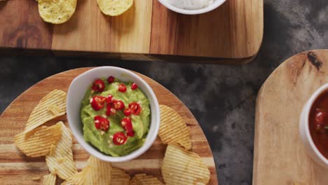 close up view of variety of chips and sauces on wooden trays on black surface