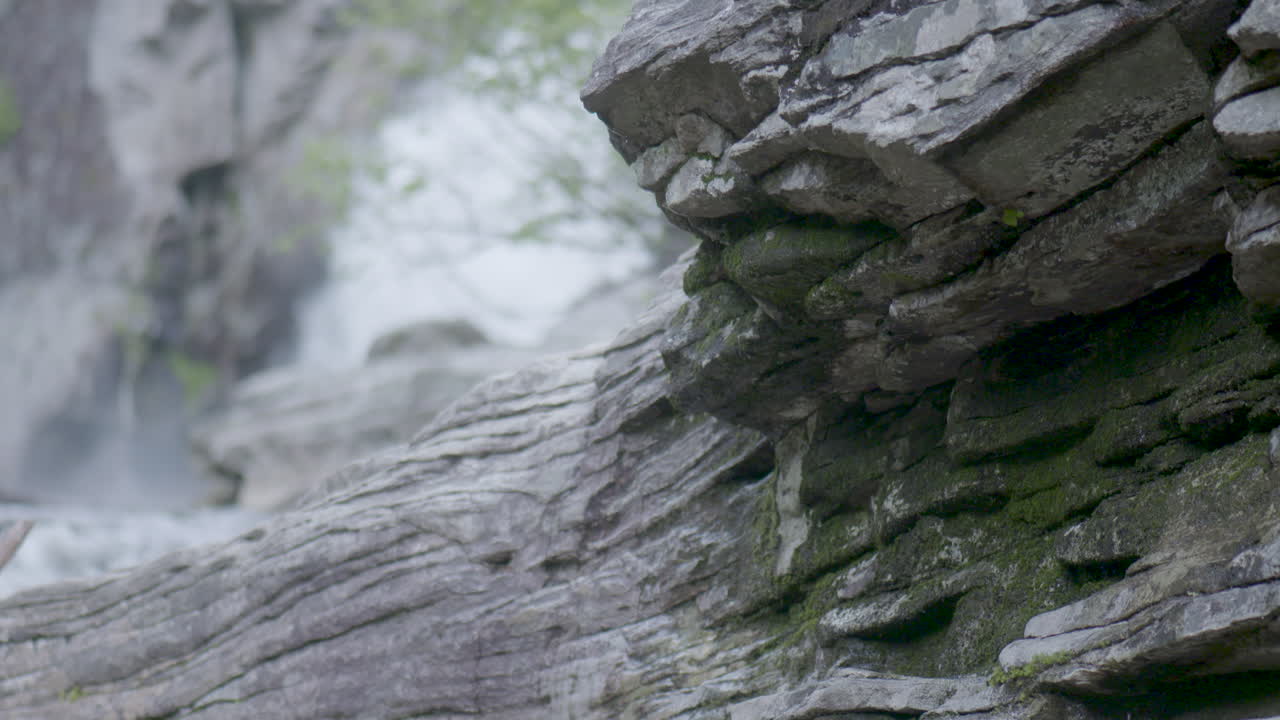 이끼 낀 바위에서 물이 뚝뚝 떨어지고, 바위 뒤로는 폭포가 쏟아지는 모습이에요