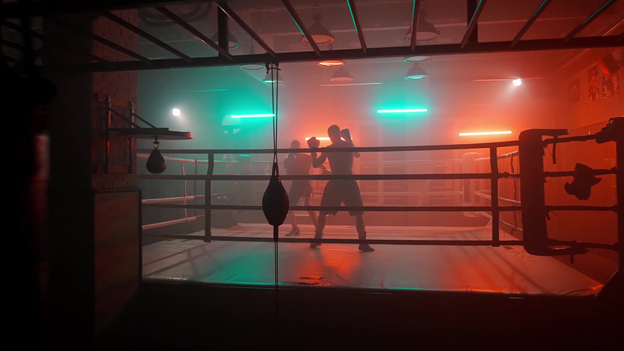 Silhouetten von Boxern beim Training in einem dunklen Boxring mit Neonlichtern.