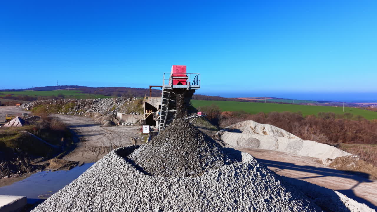 Crushed stone falling from the end of a high conveyor onto a massive pile against a clear blue sky. Aerial view of gravel falling from conveyor belt