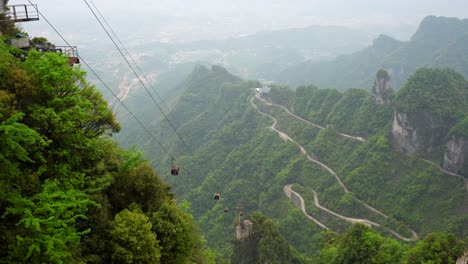 cable car glide over lush green mountains with winding roads below on a cloudy day