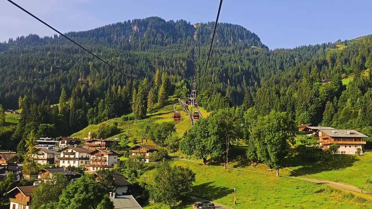Splendida vista da una gondola a Kitzbühel, Austria, che si affaccia sulla città tirolese, colline boscose, prati alpini e creste montuose distanti in una soleggiata giornata estiva di viaggio in Europa