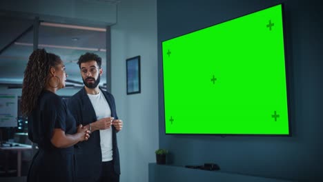 el gerente de operaciones de la compañía tiene una presentación de la reunión para el ceo. hombre adulto usa un televisor ancho con pantalla verde horizontal. la gente trabaja en la oficina de negocios.