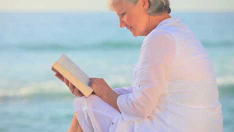 mujer madura sentada leyendo en una playa