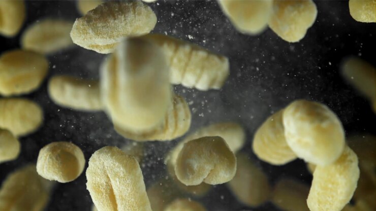 Gnocchi freschi che cadono in super slow motion su sfondo nero.