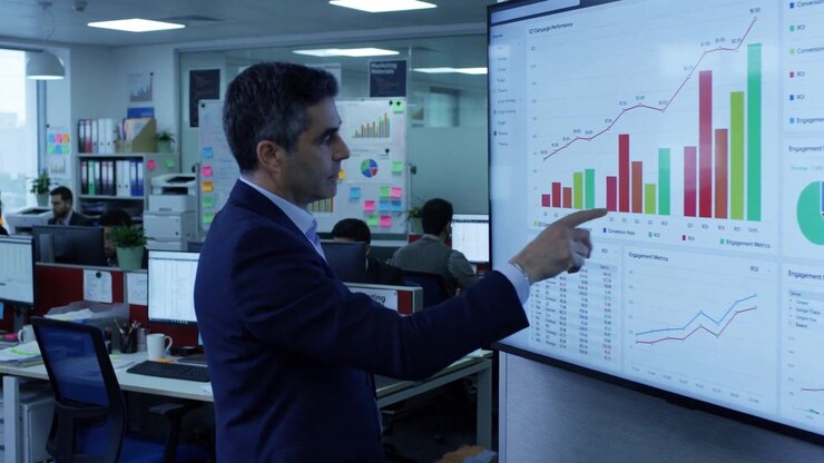 Businessman Presenting Data Charts on Large Screen in Office