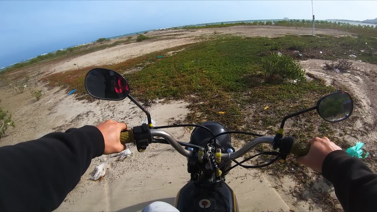 Riding motorcycle on polluted coastal part of My Hoa beach on sunny day. Vietnam. Driver POV