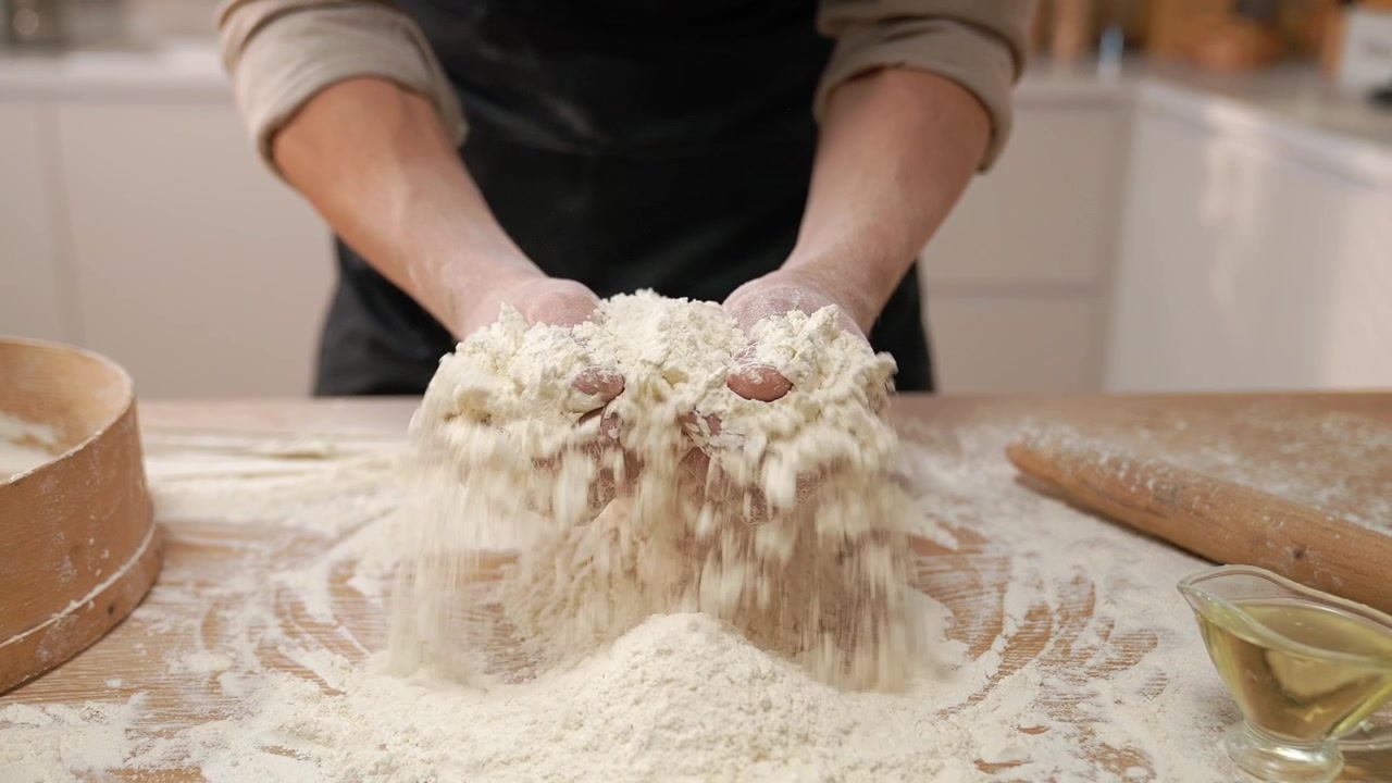 Mani dello chef che setacciano farina bianca su un tavolo da cucina di legno