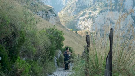 slow motion upward tracking white shot of youn asian adult male walking down dry stony path in beautiful mountain valley
