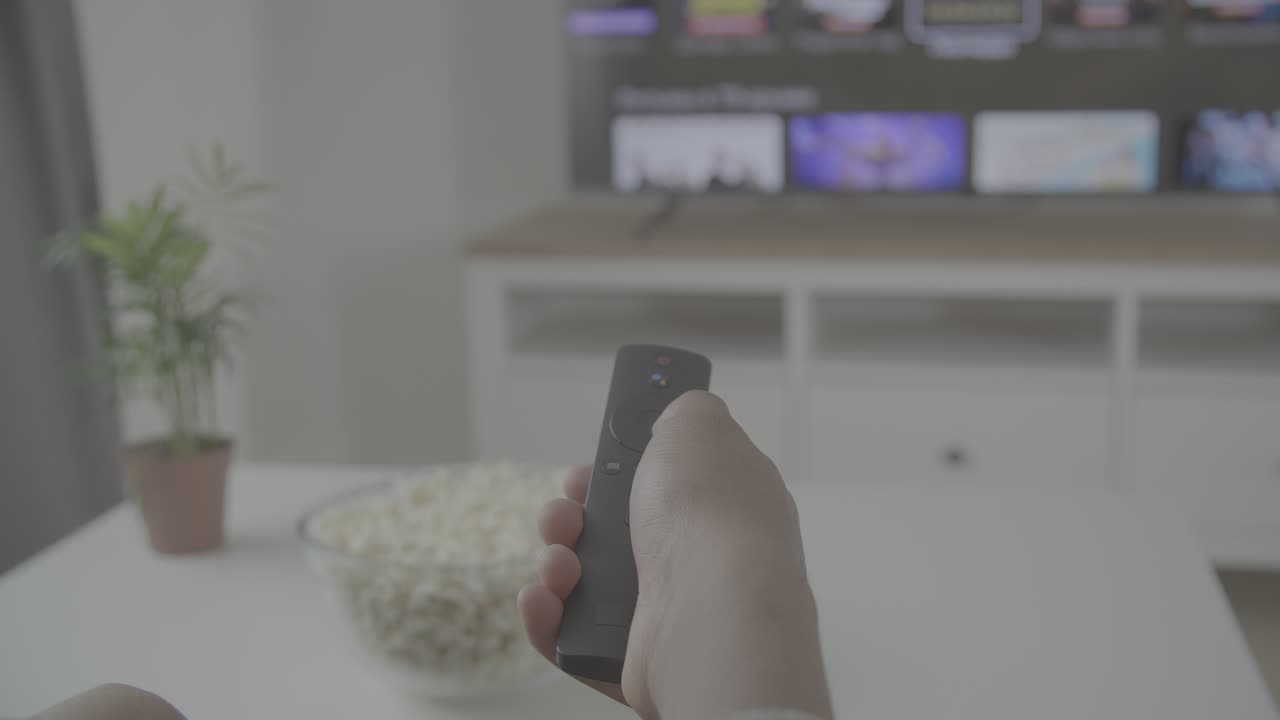 Someone's hand with a remote control navigates through the TV menu for a programme or film to watch