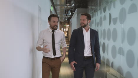 two young businessmen walking through the corridors of an office building discussing company matters