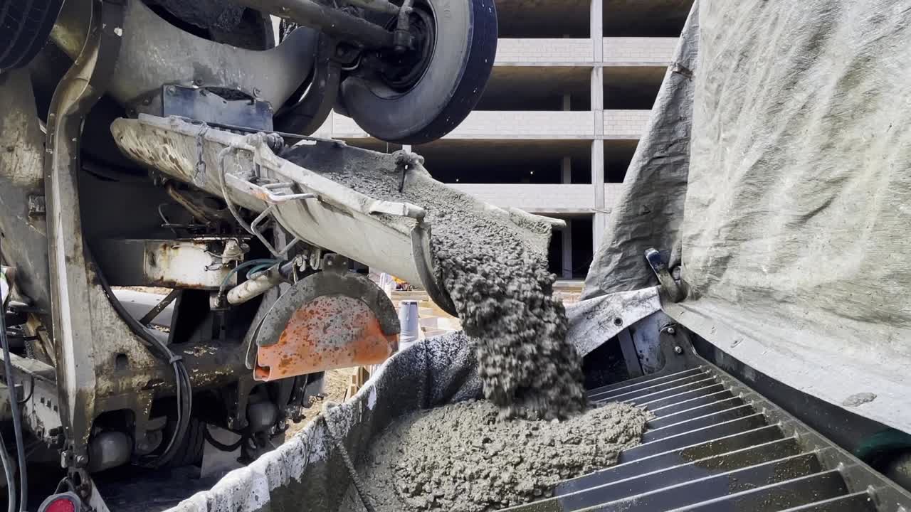 HD footage capturing a concrete truck dumping wet concrete into a concrete pump at an active construction site.