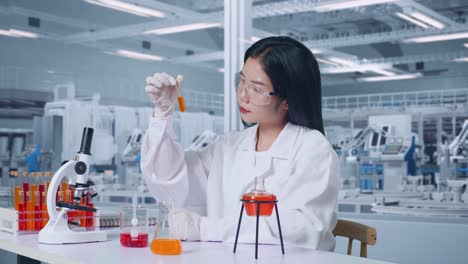 side view of asian woman scientist looking at the orange liquid in the test tube carefully while working with microscope in the laboratory, working in the lab analyzing samples test tube