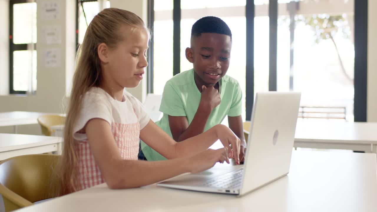 Diverse child peers girl initiating by typing, working at school desk with laptop for class project