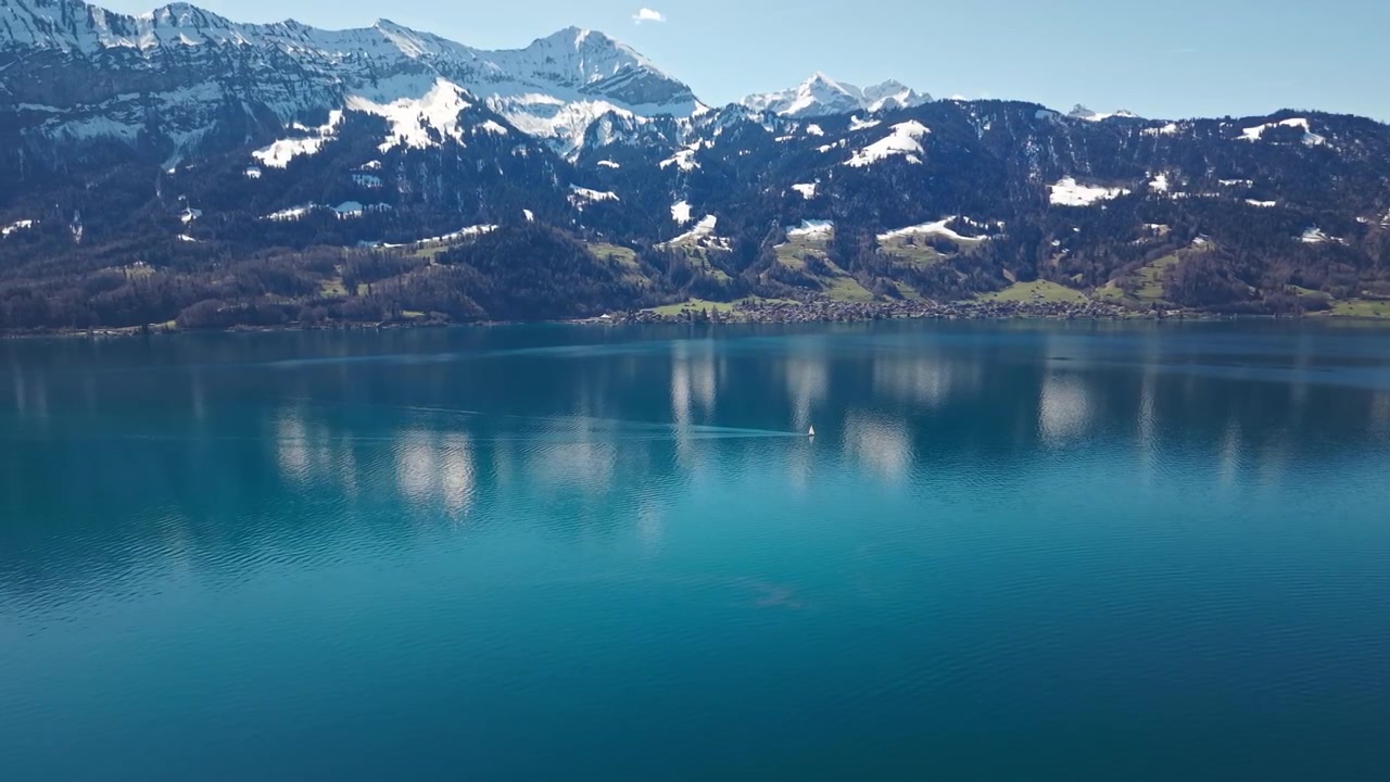 Vue aérienne du lac de Brienz avec les Alpes enneigées se reflétant sur l'eau turquoise.