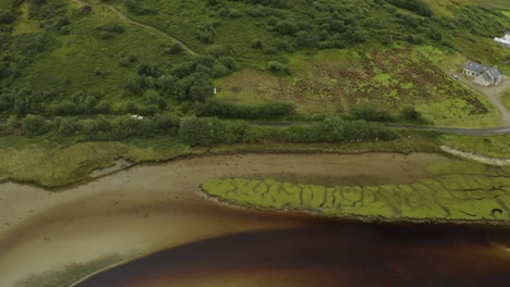 Aerial-of-small-white-car-traveling-along-road-next-to-a-river-in-Ireland