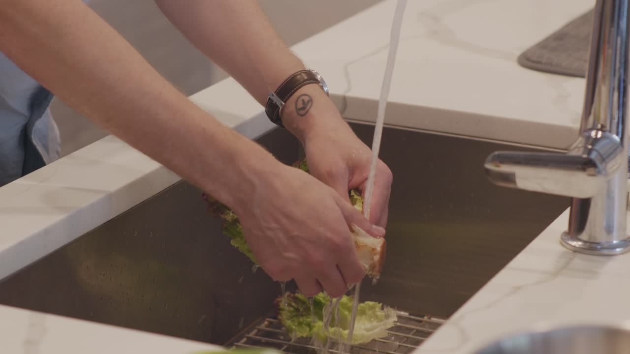 A closeup of hands washing and peeling lettuce in a kitchen sink in prep for a salad. Clean modern countertop and stainless steel faucet