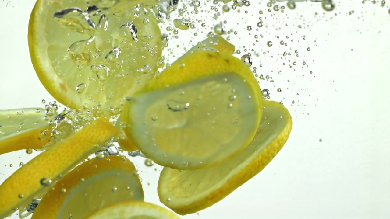 Fette di limone che cadono nell'acqua con bolle al rallentatore
