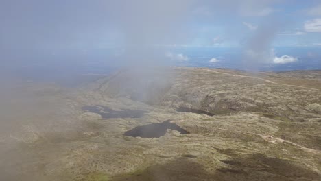 In-slow-motion,-an-aerial-perspective-captures-the-lake-atop-Portugal's-highest-point-in-the-Serra-de-Estrella-mountain-range,-with-cloud-formations-and-a-clear-blue-sky-as-the-backdrop