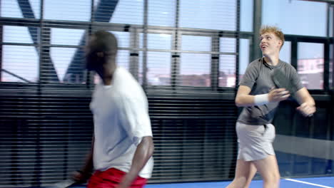 two diverse men walking on padel on indoor court holding rackets, ready for match