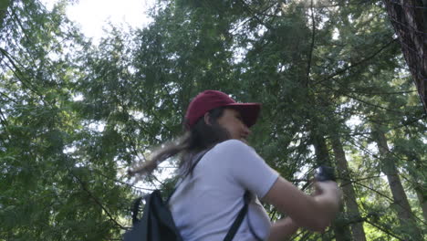 an excited, young woman having fun spinning in circles and taking a video with her camera in the forest