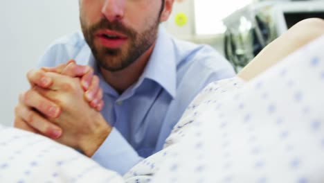 médico examinando a una mujer embarazada durante el parto mientras el hombre la sostiene de la mano en la sala de operaciones