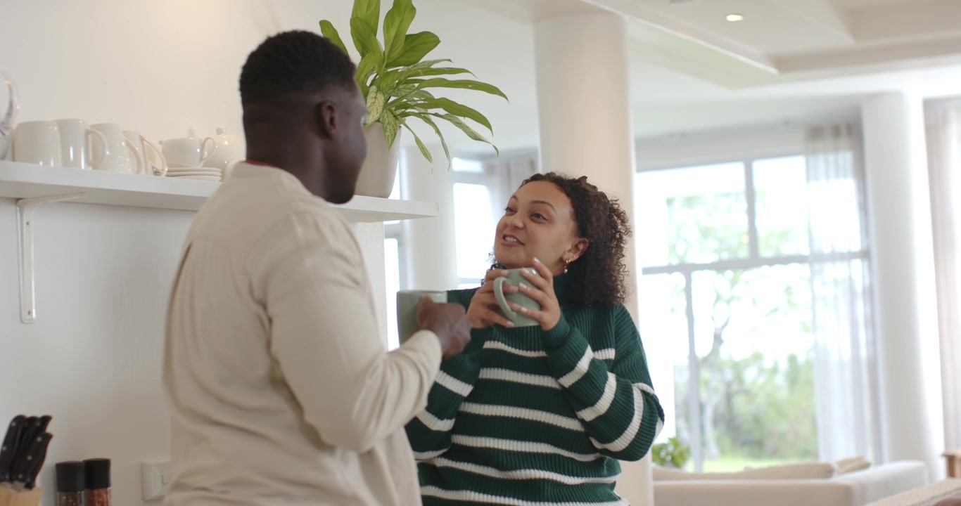 Couple afro-américain levant des tasses, buvant ensemble dans une cuisine lumineuse tout en conversant.