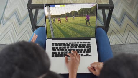 Hands-using-laptop-with-diverse-male-soccer-players-playing-match-on-screen