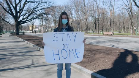 woman holding a stay at home sign in a park during a pandemic