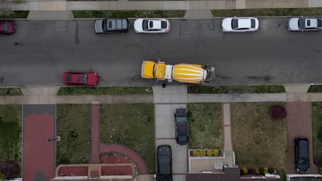 A-top-down-view-high-over-a-yellow-and-white-cement-truck-in-a-residential-neighborhood-on-a-cloudy-day