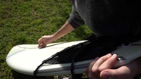 detail of the hands of a surfer applying wax on the surface of the board